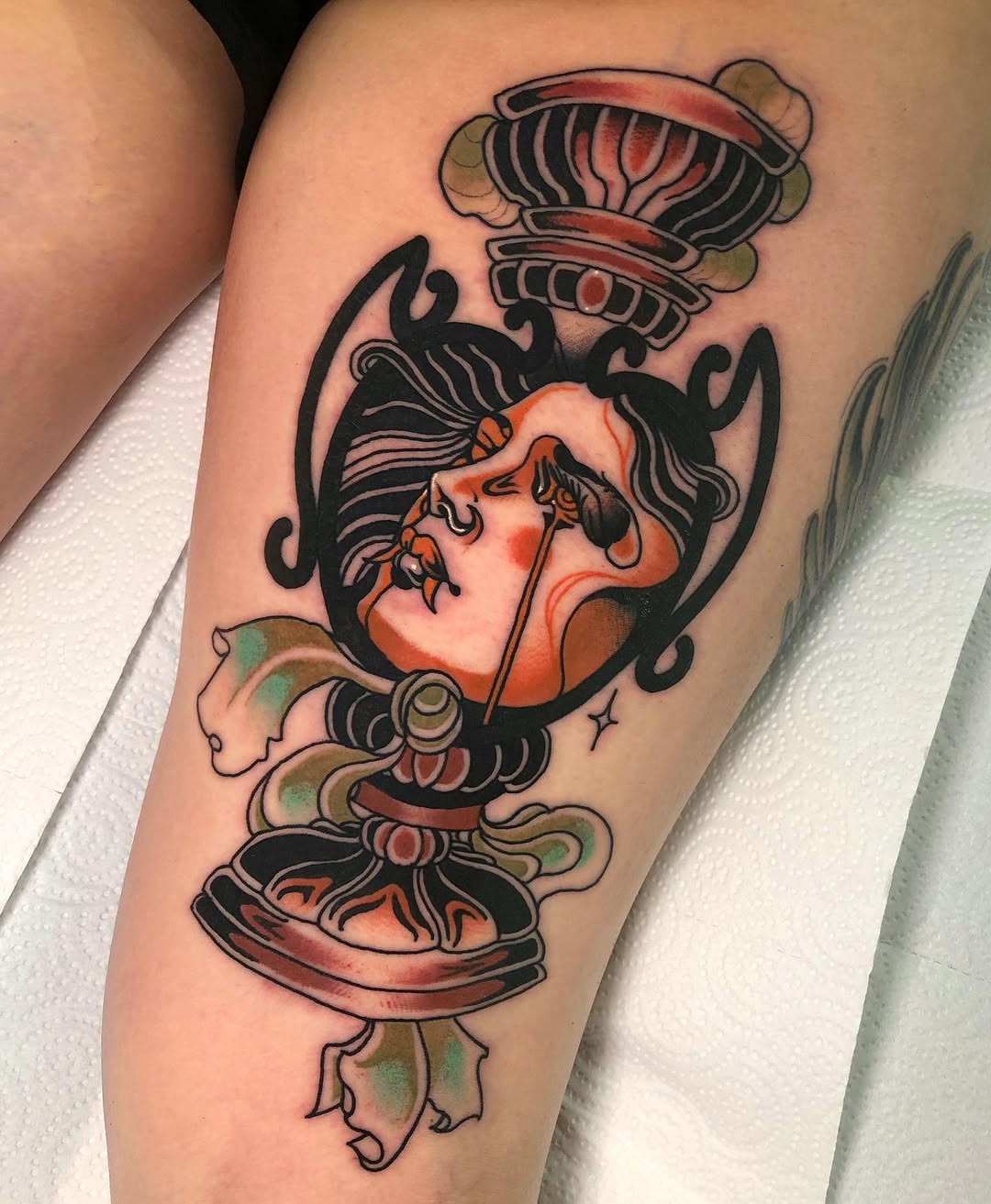 Colorful portrait tattoo of a woman's head with black hair and ornate decorative elements in red, orange, and green tones on the upper arm.