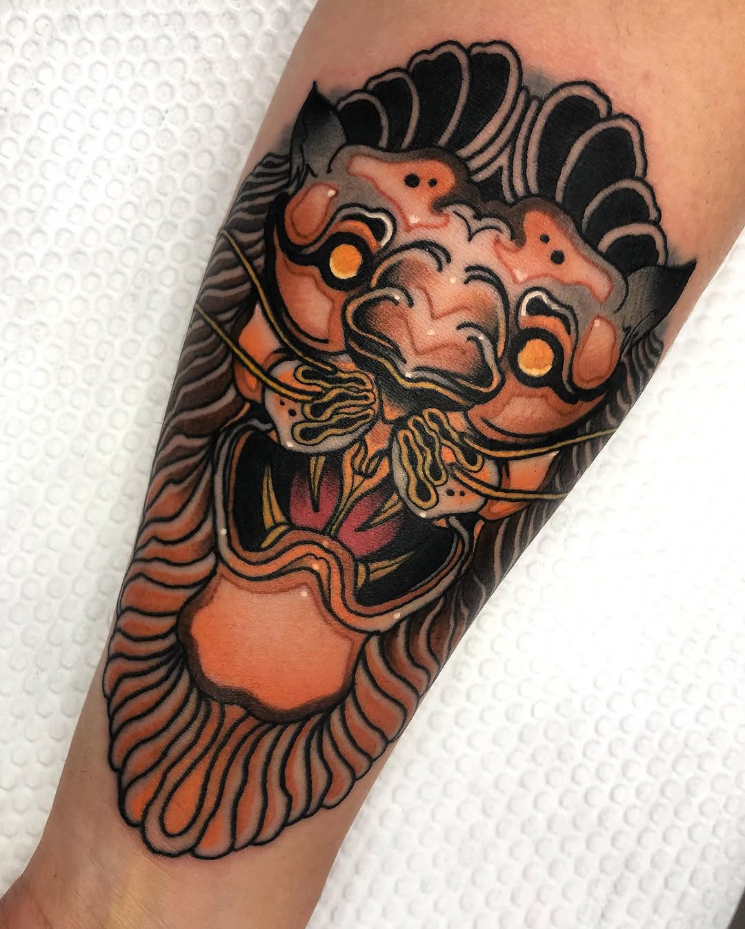 Colorful orange and black lion head tattoo with decorative mane and ornamental details on a forearm.