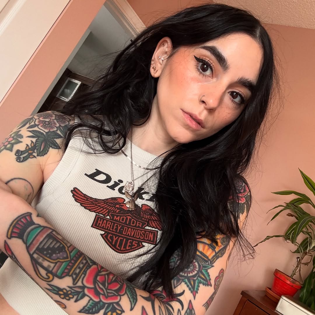 Woman displaying colorful floral and eagle tattoos on both shoulders and arms in red, green, and blue ink.