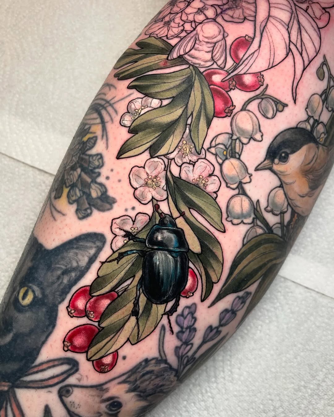 Colorful arm tattoo featuring botanical elements including red berries, pink flowers, green leaves, and a black beetle among various flora designs.