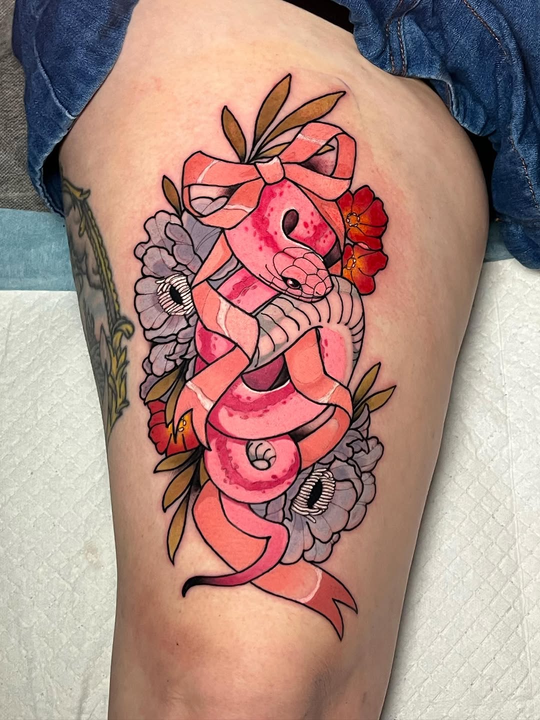 Colorful coral and pink snake with a red bow surrounded by purple and red flowers on the thigh, featuring watercolor shading effects.