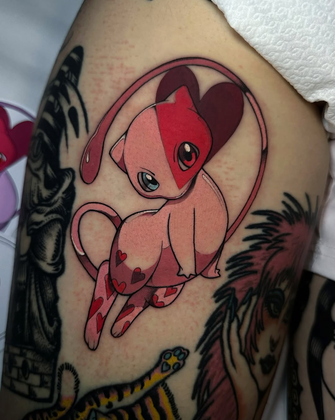 Red and pink cartoon character with heart-shaped markings on legs, displayed on upper arm with surrounding black detailed designs.