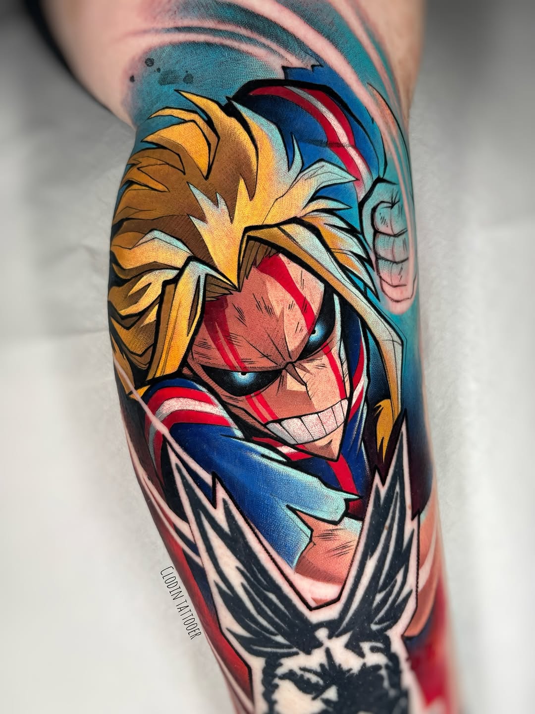 Colorful tattoo on a leg featuring a character with spiky blonde hair, red and blue striped clothing, and an expressive face against a turquoise background.