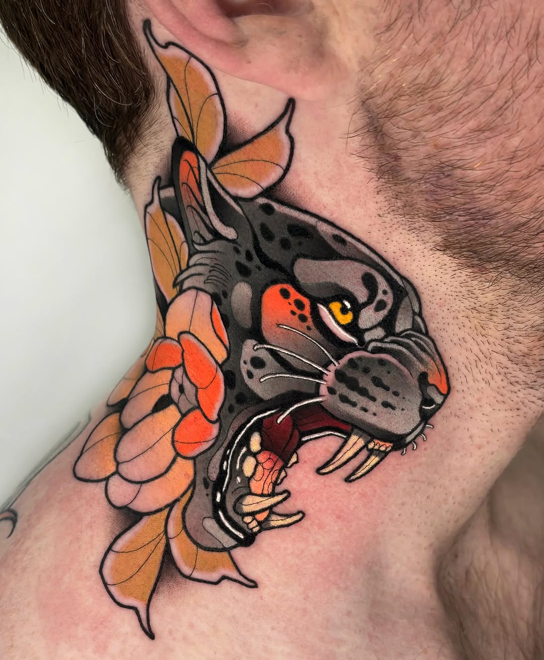 Colorful neck tattoo featuring a dark rat with red eyes and yellow fangs beside an orange flower with petals.