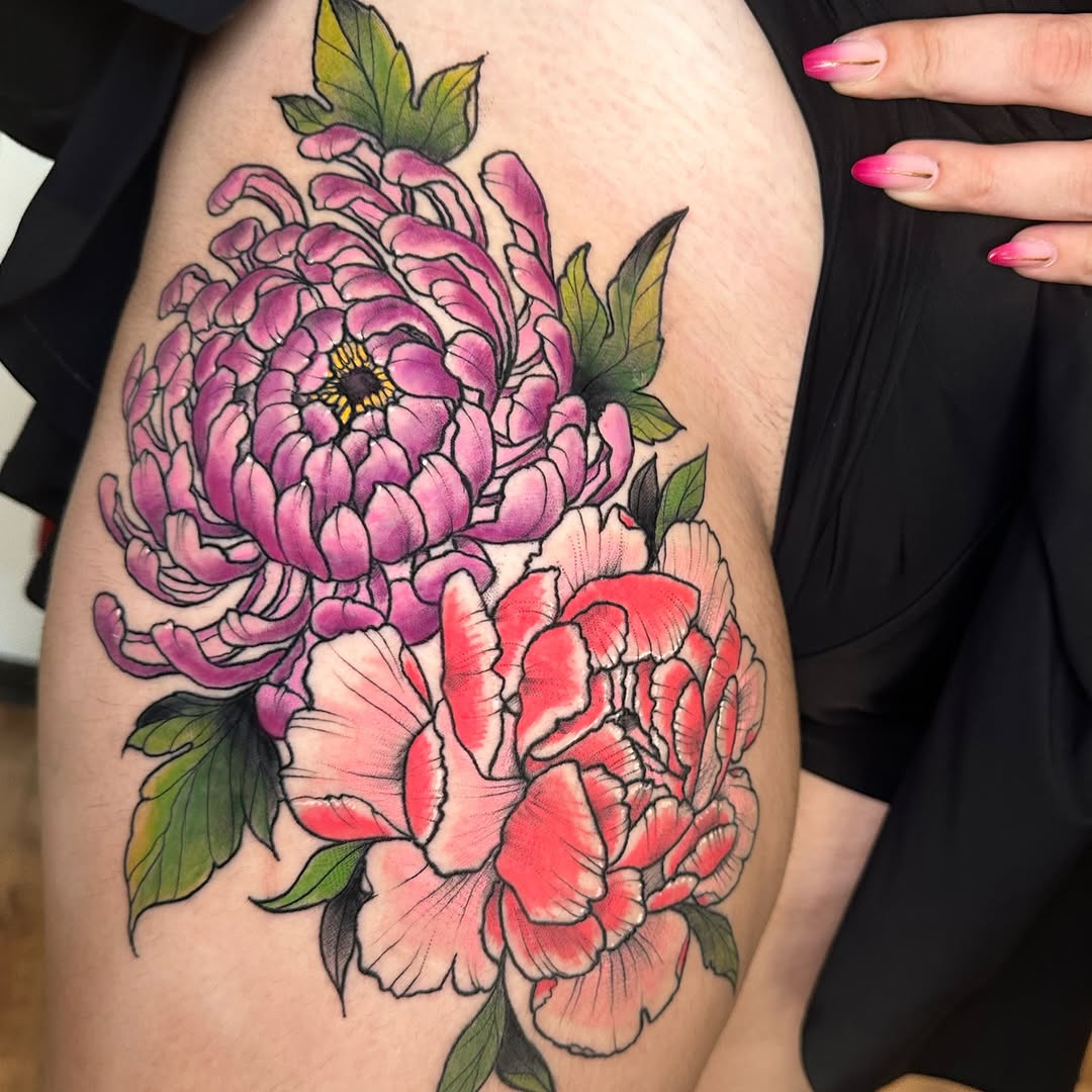 Colorful peony flower tattoo on thigh featuring pink and red blooms with green leaves and yellow center detail.