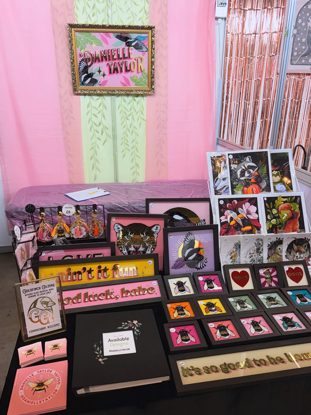 Danielle Taylor's tattoo portfolio display featuring colorful flash sheets with bees, animals, flowers, and hearts in pink, black, and gold framed designs.