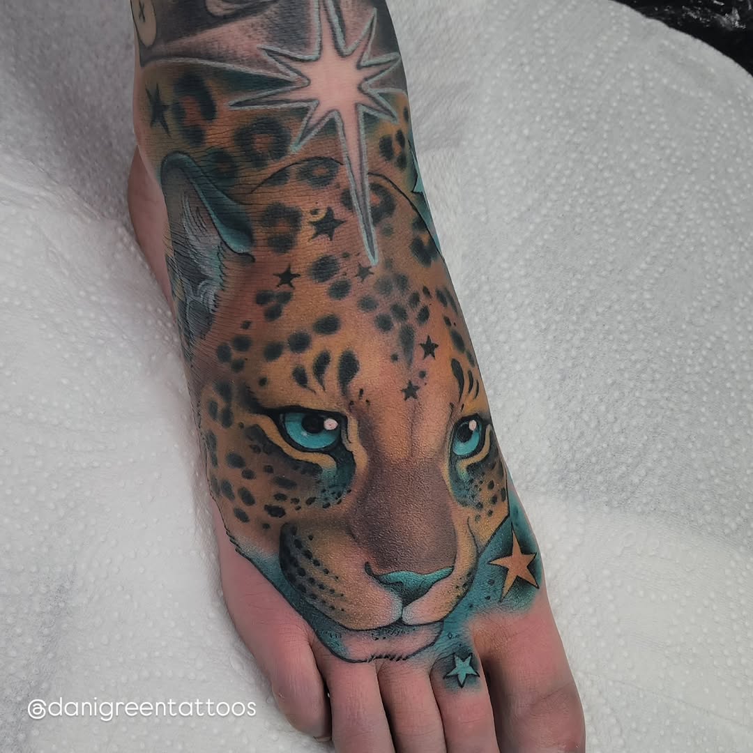 Leopard head with turquoise eyes and scattered stars tattooed on the foot and lower leg in brown and teal colors.