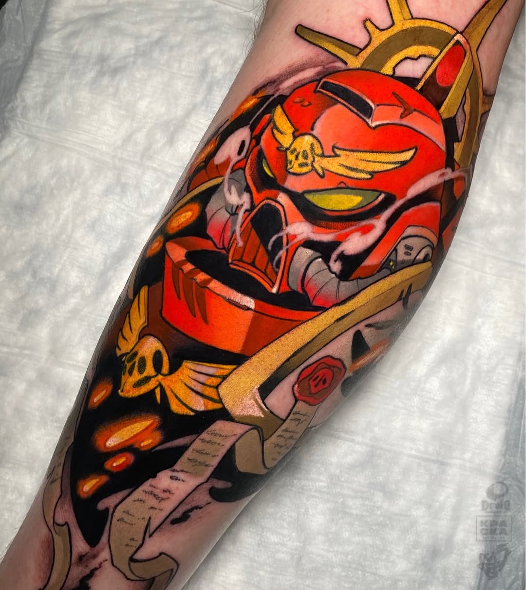 Colorful tattoo on a calf featuring a red robot character with golden accents, wings, and mechanical details surrounded by orange flames and scrolls.
