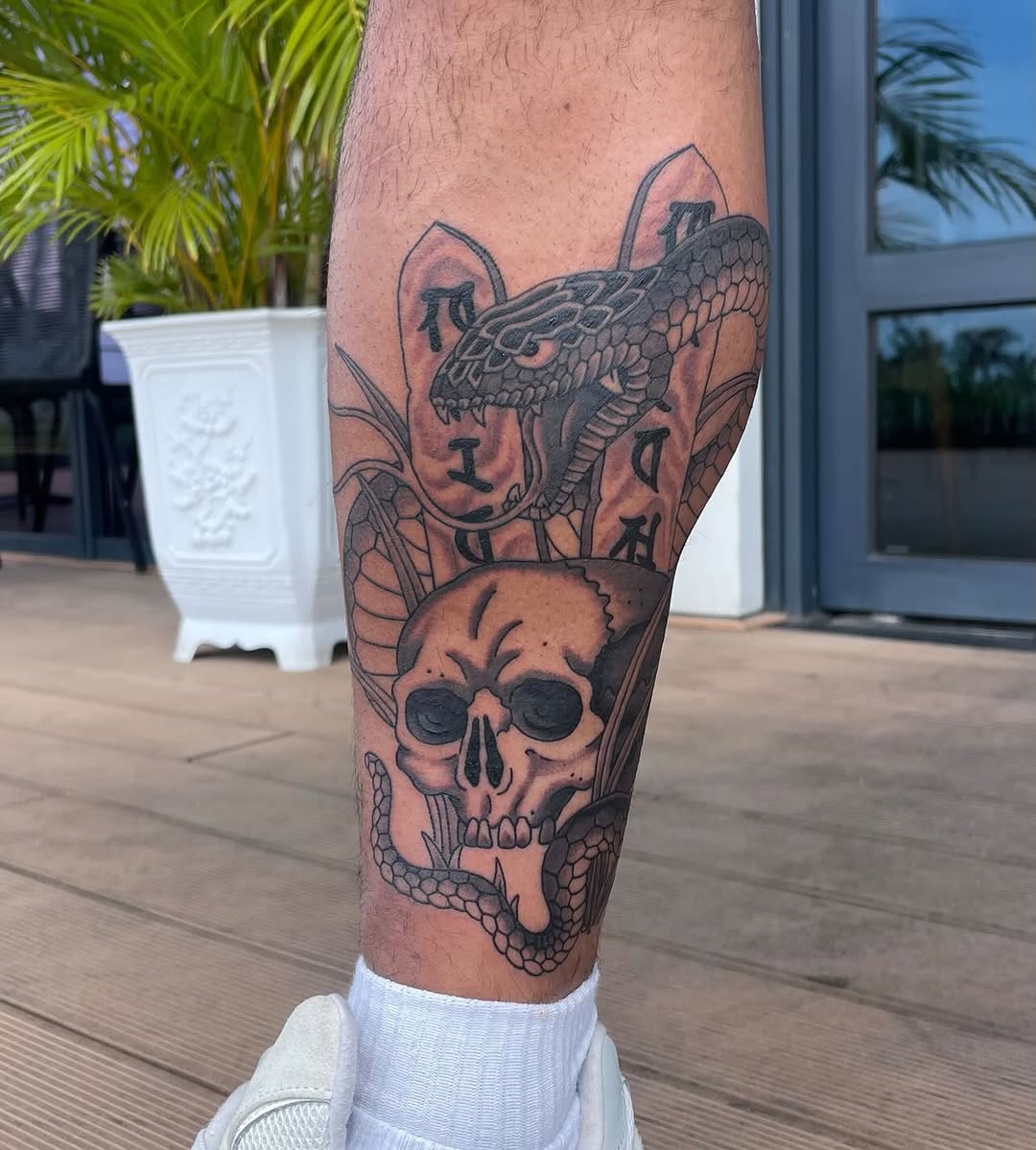 Leg tattoo featuring a skull with sunglasses, a coiled snake, a lizard head, and decorative botanical elements in black and gray ink.