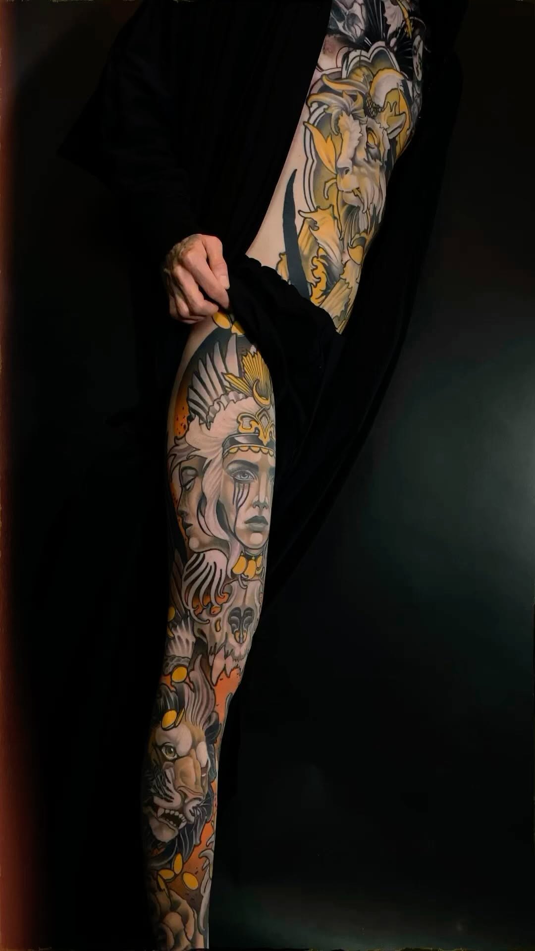Full-length arm tattoo sleeve featuring classical portrait heads, ornamental details, and gold accents on a person's arm against a black background.