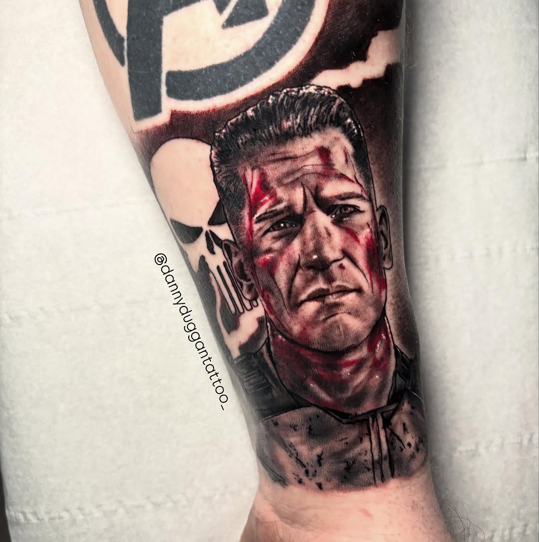 Detailed portrait tattoo on forearm depicting a man's face with red and black ink, featuring sharp facial features and a serious expression.