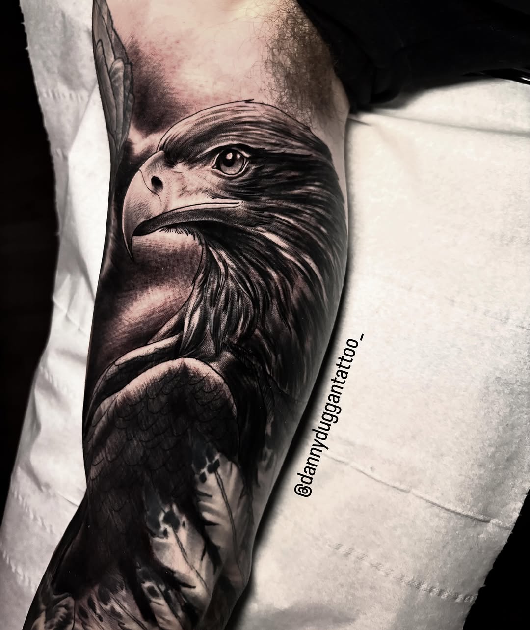Detailed eagle head tattoo on the inner forearm with intricate feather work and shading in black ink.