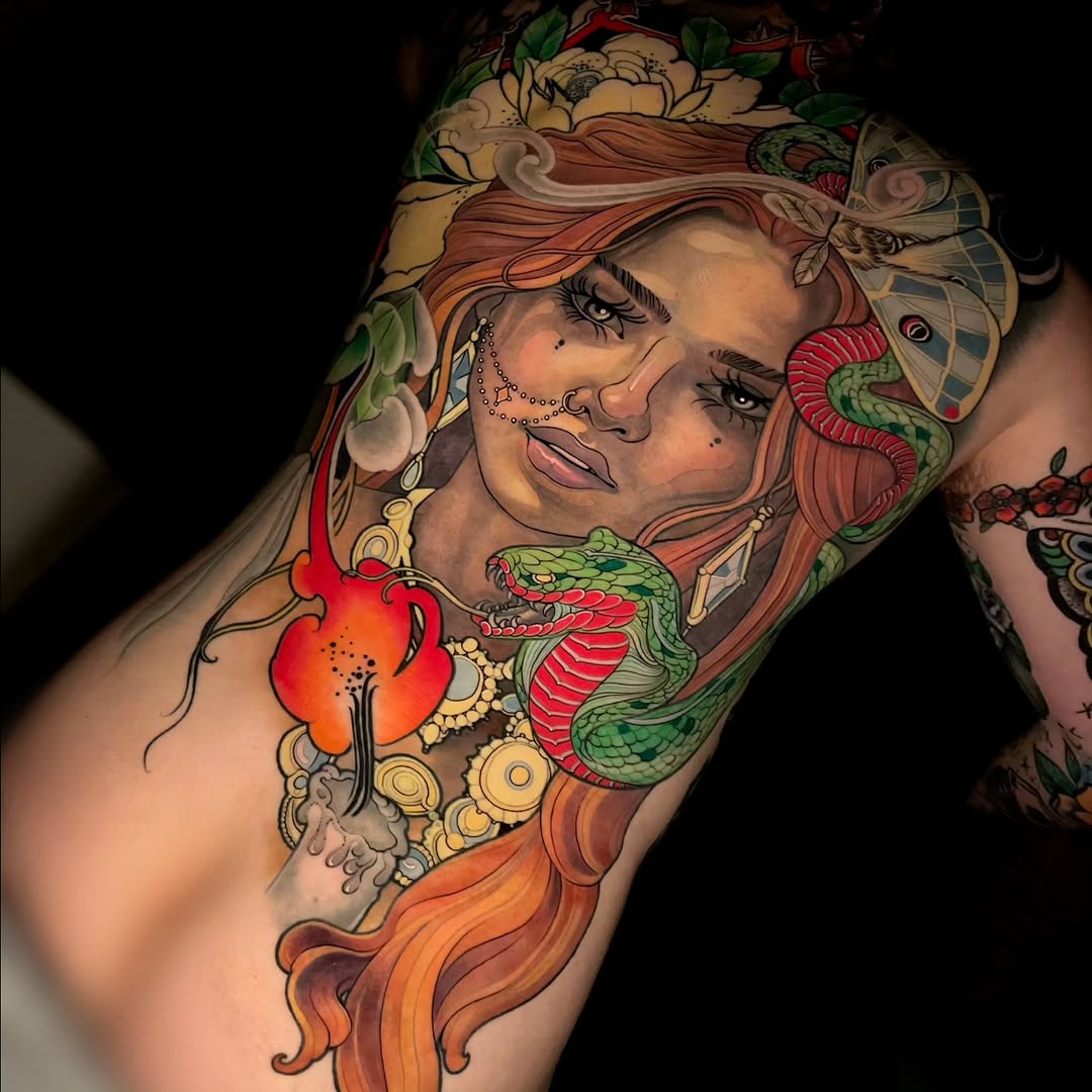 Colorful shoulder tattoo featuring a woman with orange-red hair, adorned with flowers, a green snake, red flower, and gold jewelry details.