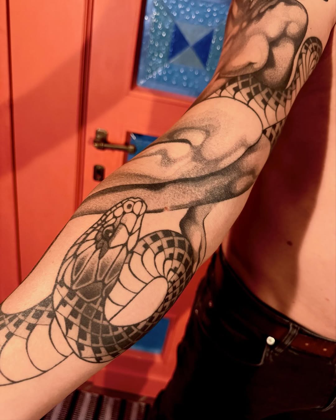 Detailed winged serpent tattoos covering both forearms with geometric patterns, displayed against a red and blue interior background.