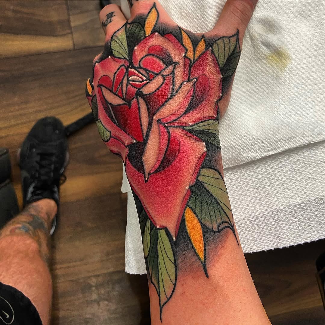 Large red rose with green and yellow leaves covering the back of the hand and forearm, outlined in black with detailed shading and color work.