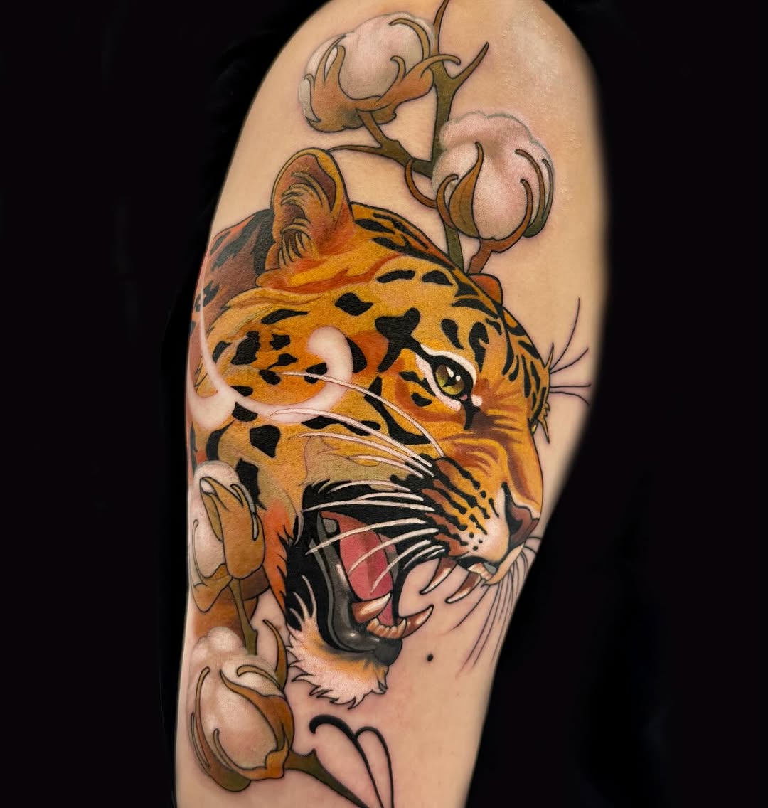 Roaring leopard head with open mouth and spotted coat in orange and black, surrounded by cotton plant stems on upper arm.