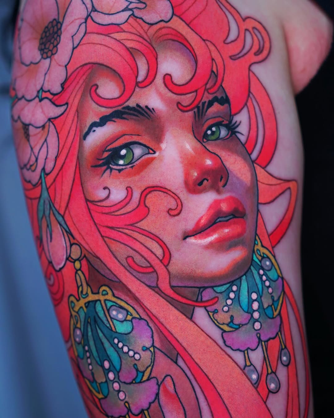 Colorful portrait tattoo of a woman with voluminous red hair, green eyes, red skin, and ornate butterfly wing earrings on the upper arm.