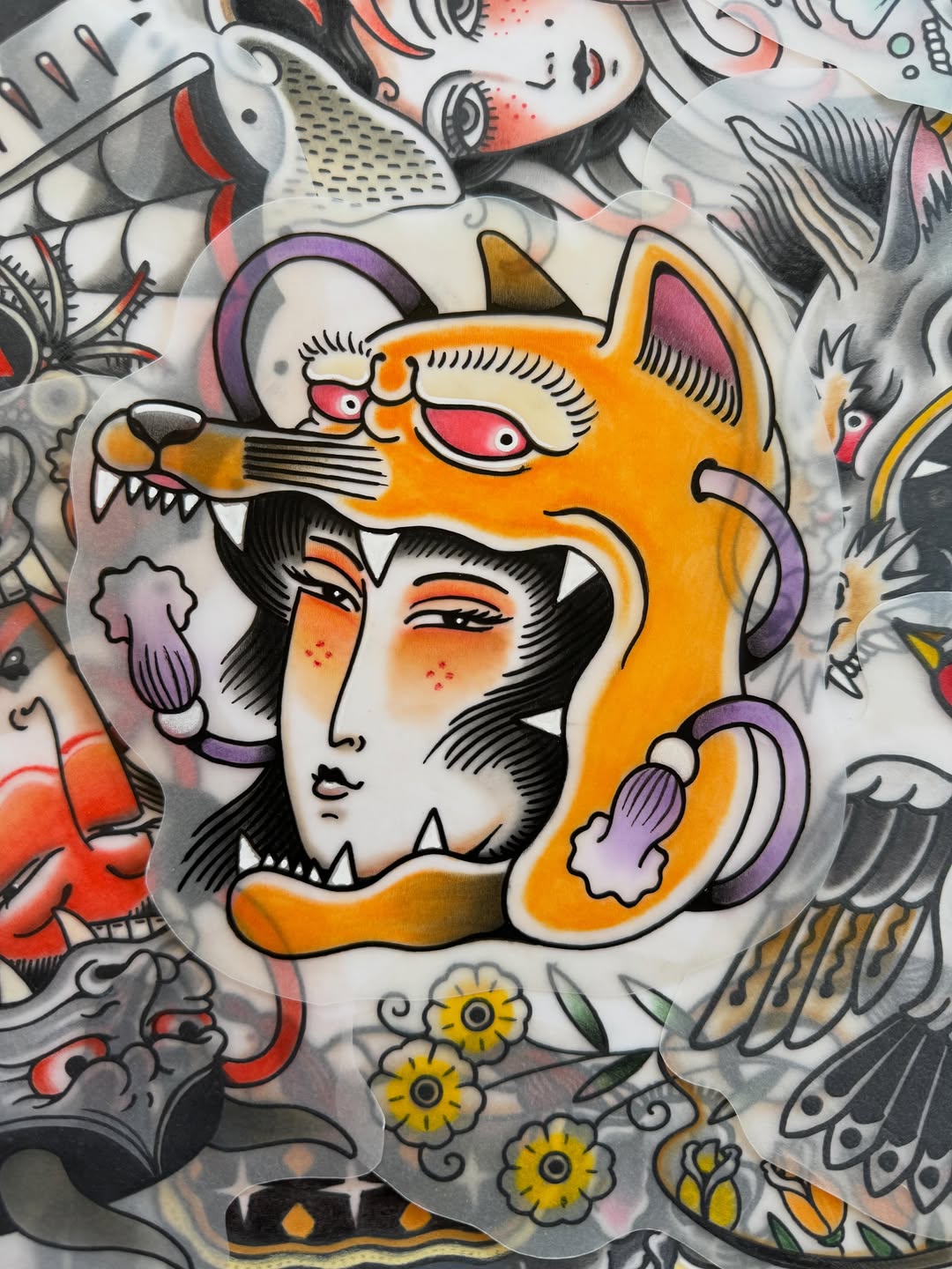 Colorful shoulder tattoo featuring an orange cat-headed figure with a human face, surrounded by flowers, fish, and decorative elements in orange, purple, and black.