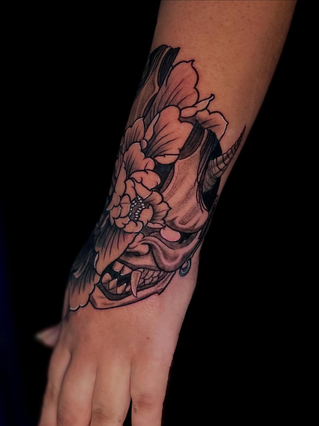 Colorful skull with flowers and wings tattoo on the forearm and hand, featuring pink, coral, and black ink.