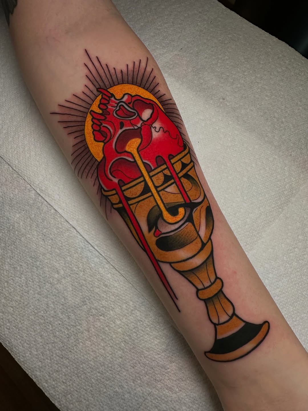 Red and gold torch with anatomical heart flames and radiating lines, tattooed on inner forearm with orange and black accents.
