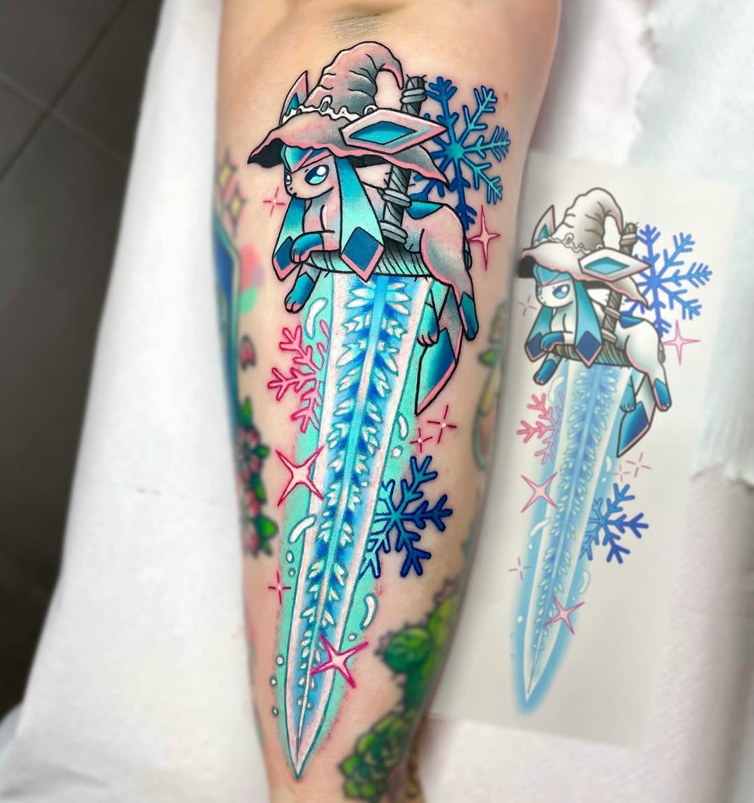 Colorful leg tattoo featuring two ice-themed mythical creatures with flowing icy tails, surrounded by snowflakes and sparkles in blue, pink, and green.