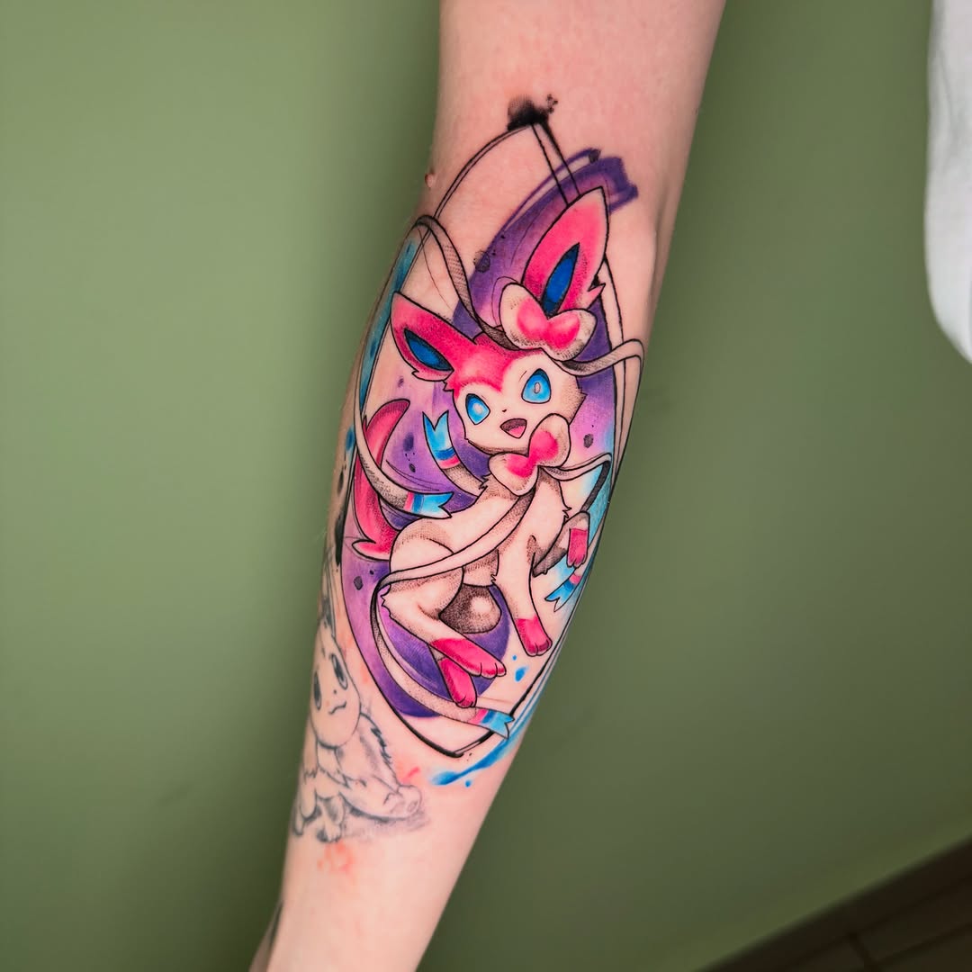 Colorful tattoo of a pink creature with blue eyes and antennae on the calf, featuring purple, pink, and blue watercolor elements with black outlines.
