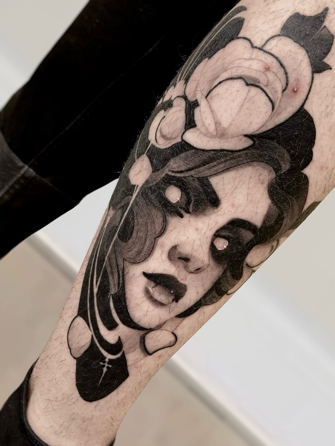 Two expressive faces stacked vertically on the forearm in black and gray ink, featuring detailed shading and emotional expressions.