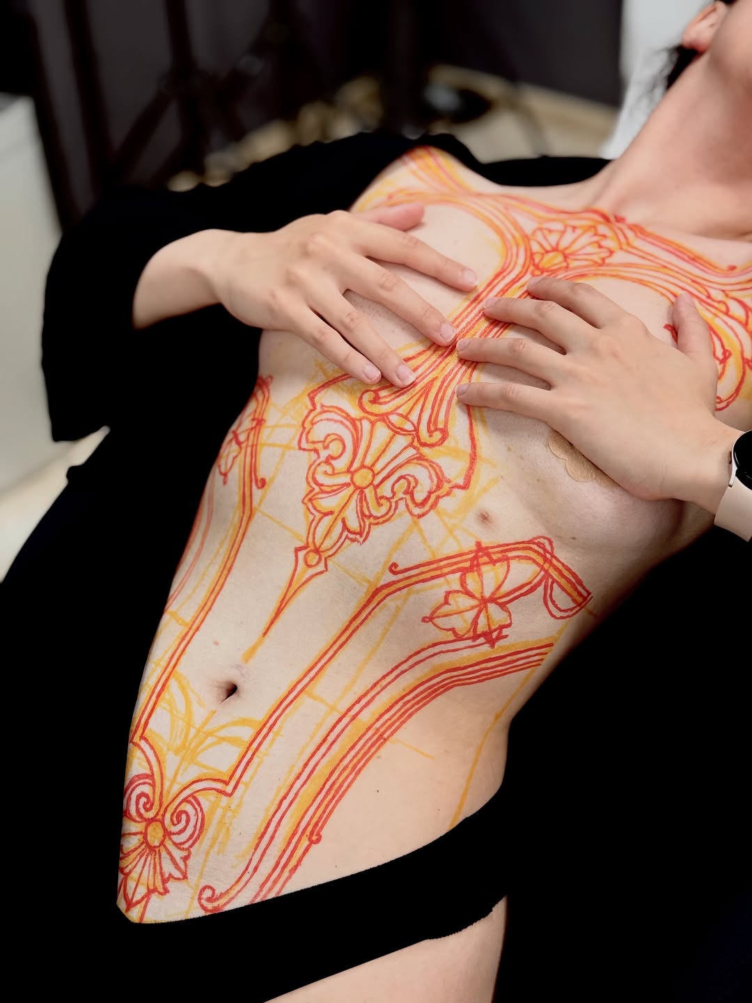 Ornate red and yellow decorative mandala-inspired tattoo covering the torso and side of a person's body.