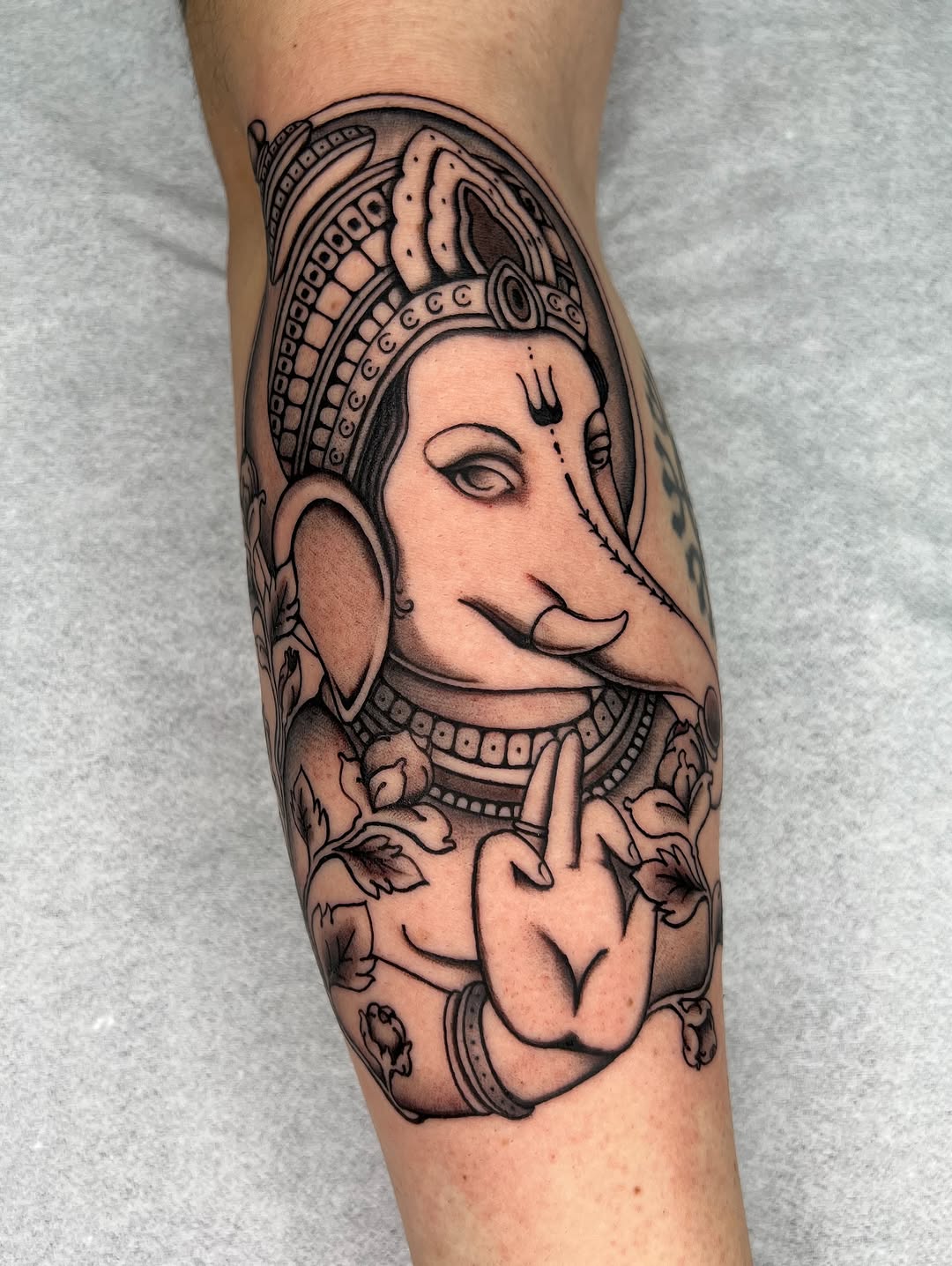 Ganesha tattoo on forearm featuring the deity with ornate headdress, jewelry, and floral elements rendered in black ink on skin.