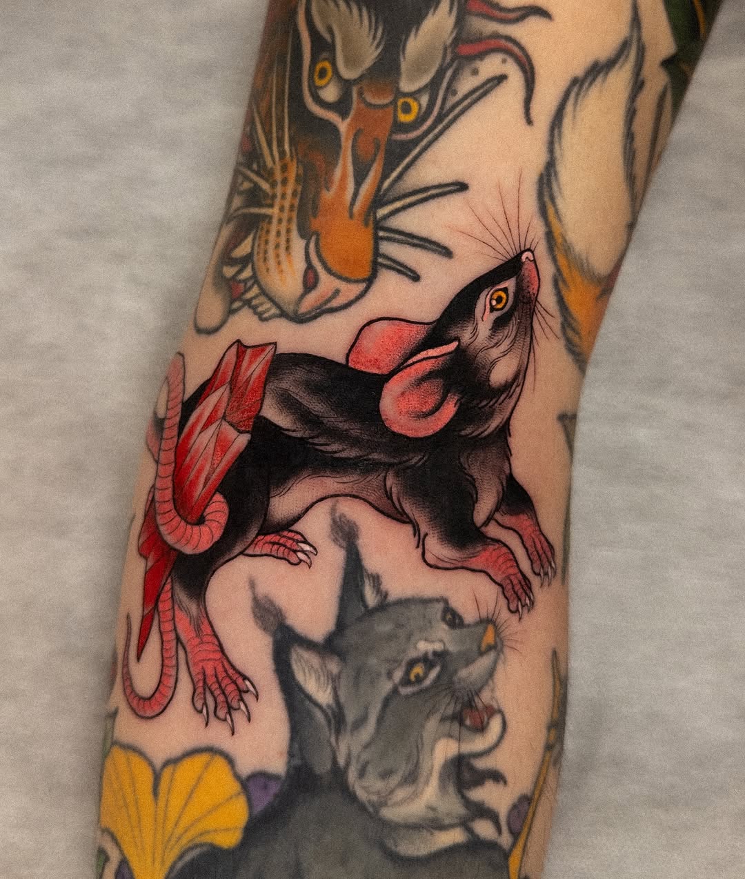 Colorful leg tattoo featuring three rats with red and black markings, yellow flowers, and cat faces with yellow eyes arranged vertically on the calf.