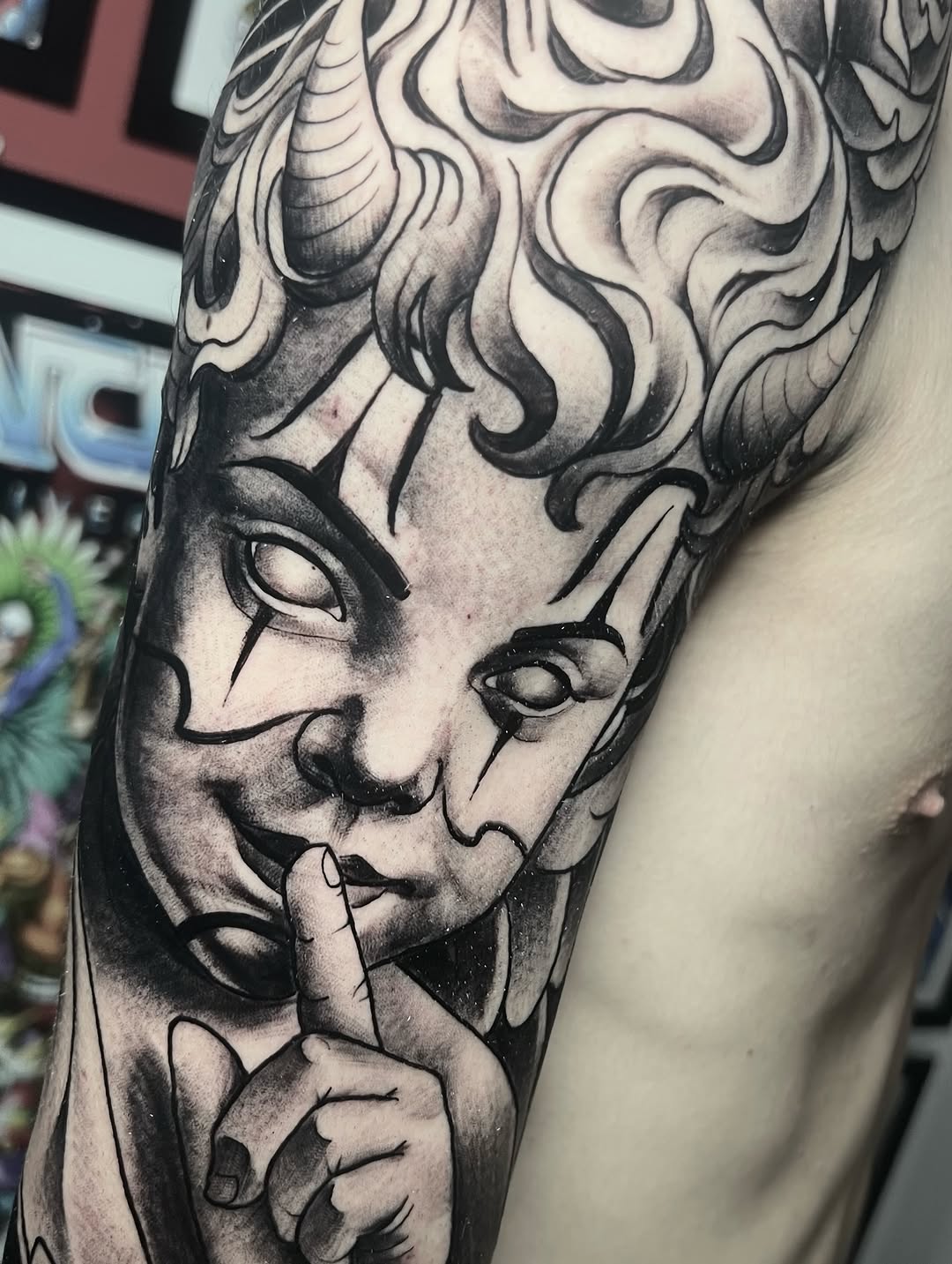 Detailed monochrome portrait tattoo on upper arm featuring a face with ornate curled hair and decorative scrollwork, rendered in black ink and shading.