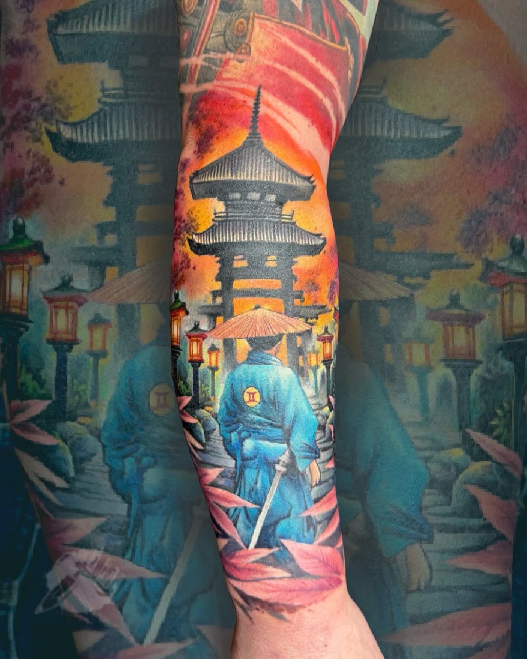 Colorful sleeve tattoo featuring an Asian pagoda and figure in blue robes holding an umbrella, surrounded by lanterns and architectural elements in red, orange, and teal tones.