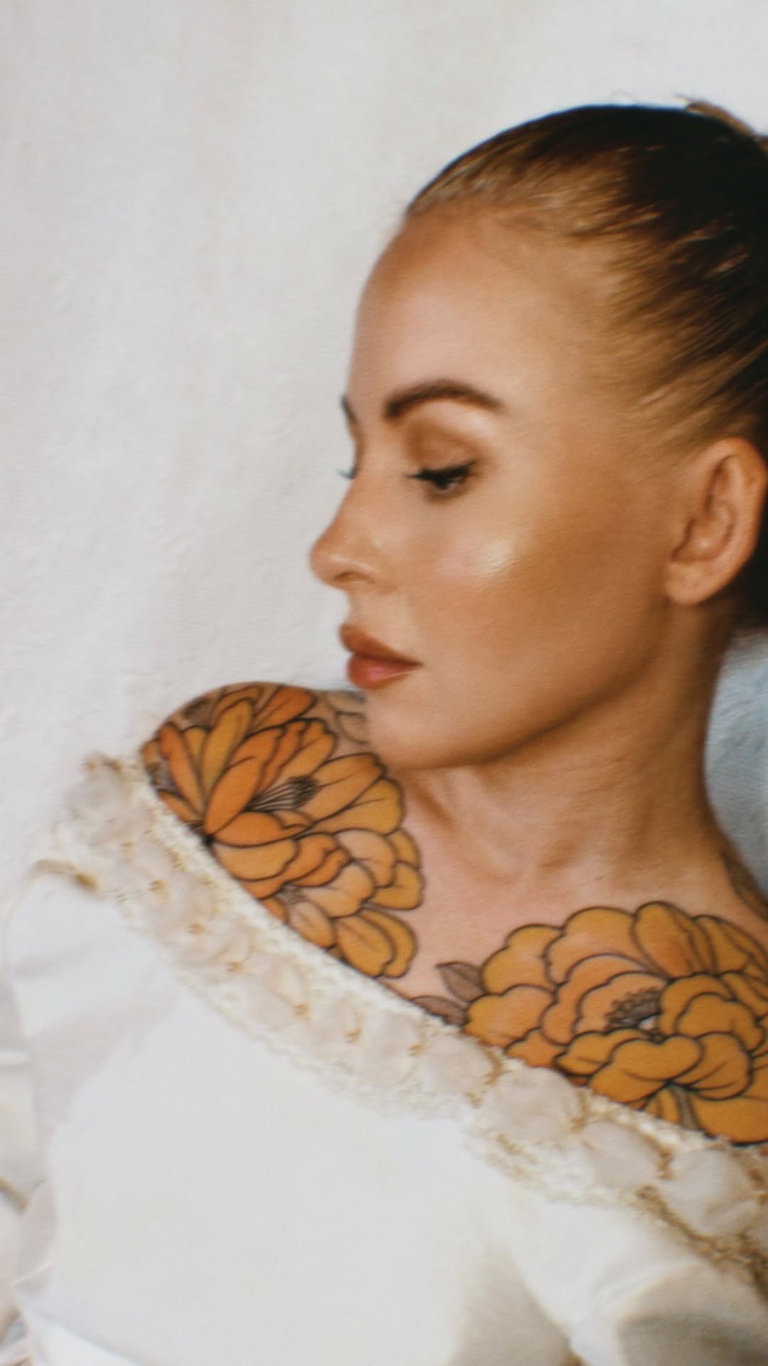 Woman in profile wearing a cream-colored garment displaying orange and black butterfly wing tattoos on her shoulders and upper back.