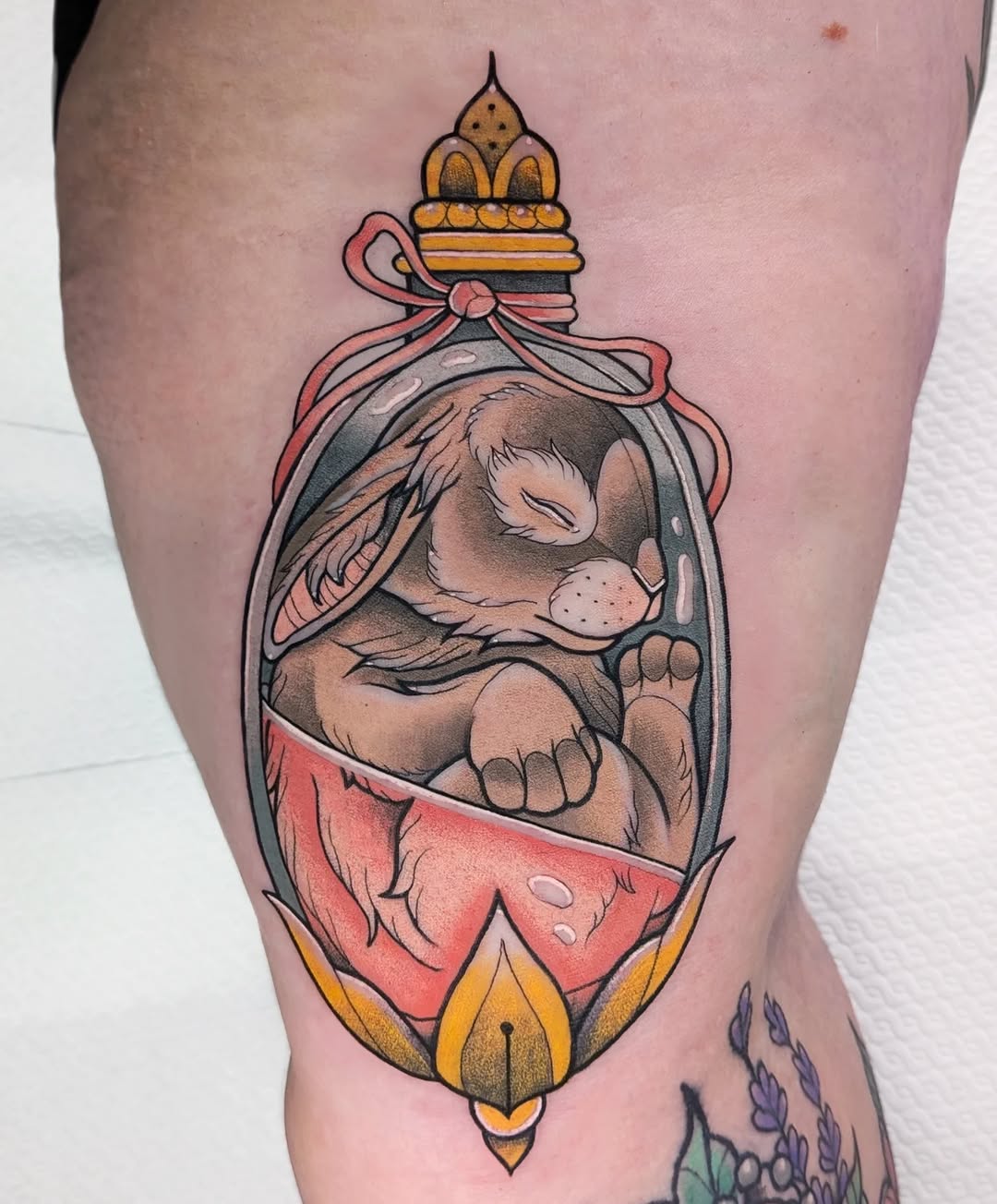 Decorative bottle tattoo on thigh featuring a sleeping animal wearing red fabric, topped with a golden crown and pink bow, surrounded by ornamental frames in red, gold, and grey.