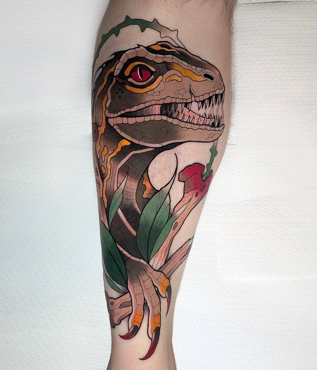 Colorful reptilian creature head with orange and green markings, sharp teeth, and red eye on a calf with botanical elements below.