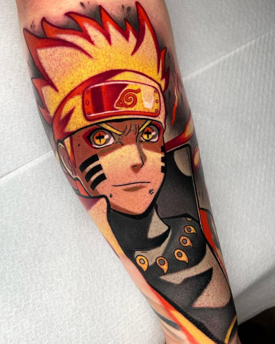 Colorful tattoo on a forearm featuring a character with spiky red and yellow hair, headband, facial markings, and black outfit with orange details.