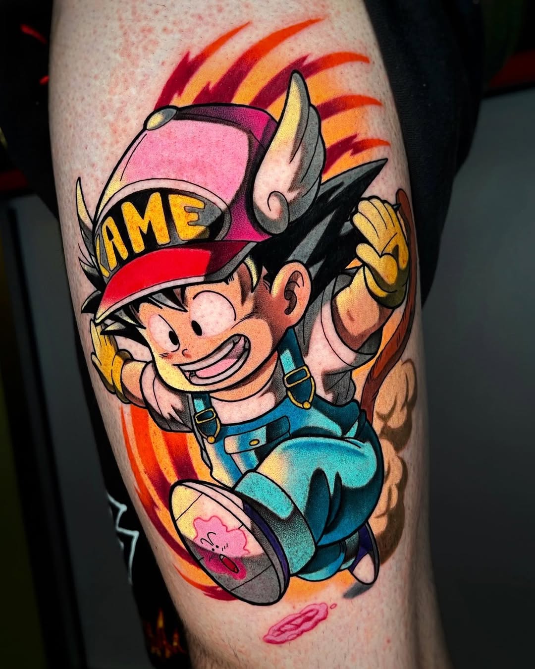Colorful tattoo on a calf featuring a smiling character with a pink and red hat, blue overalls, and large gloved hands against an orange and red flame background.