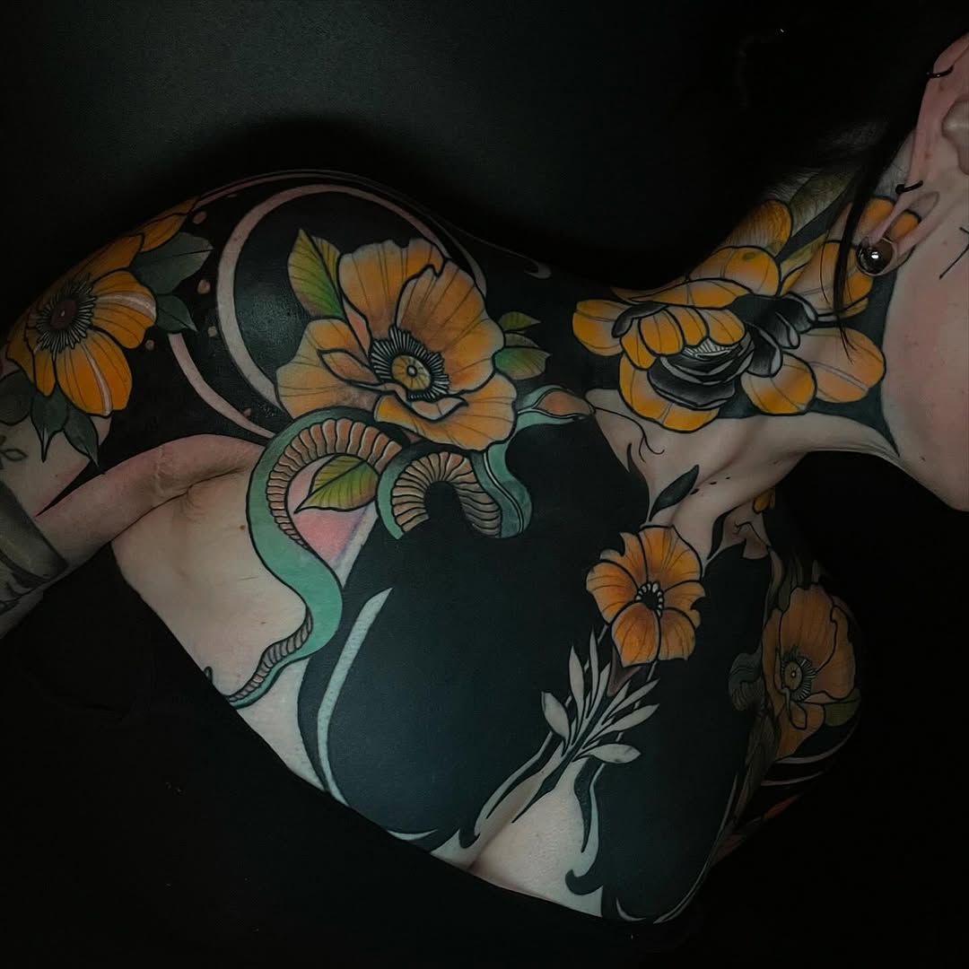Colorful chest and shoulder tattoo featuring golden yellow flowers with green leaves, a turquoise serpent, and a crescent moon on dark background skin.