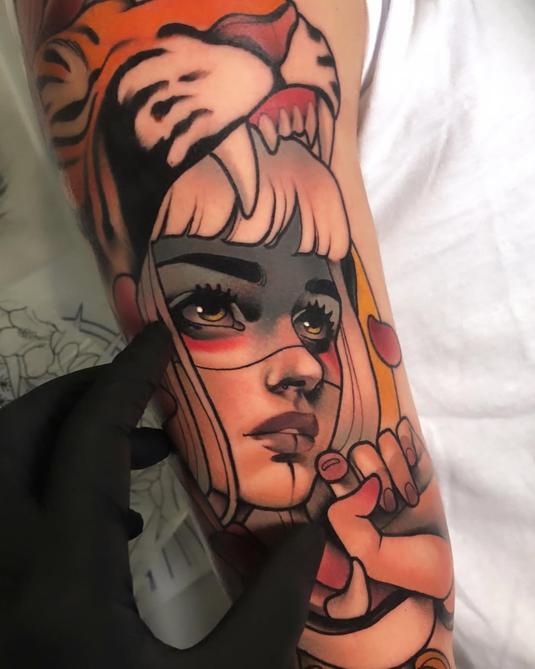 Colorful portrait tattoo on forearm featuring a woman with long blonde hair, red and orange tones, gold eyes, and decorative elements including flowers and circular details.