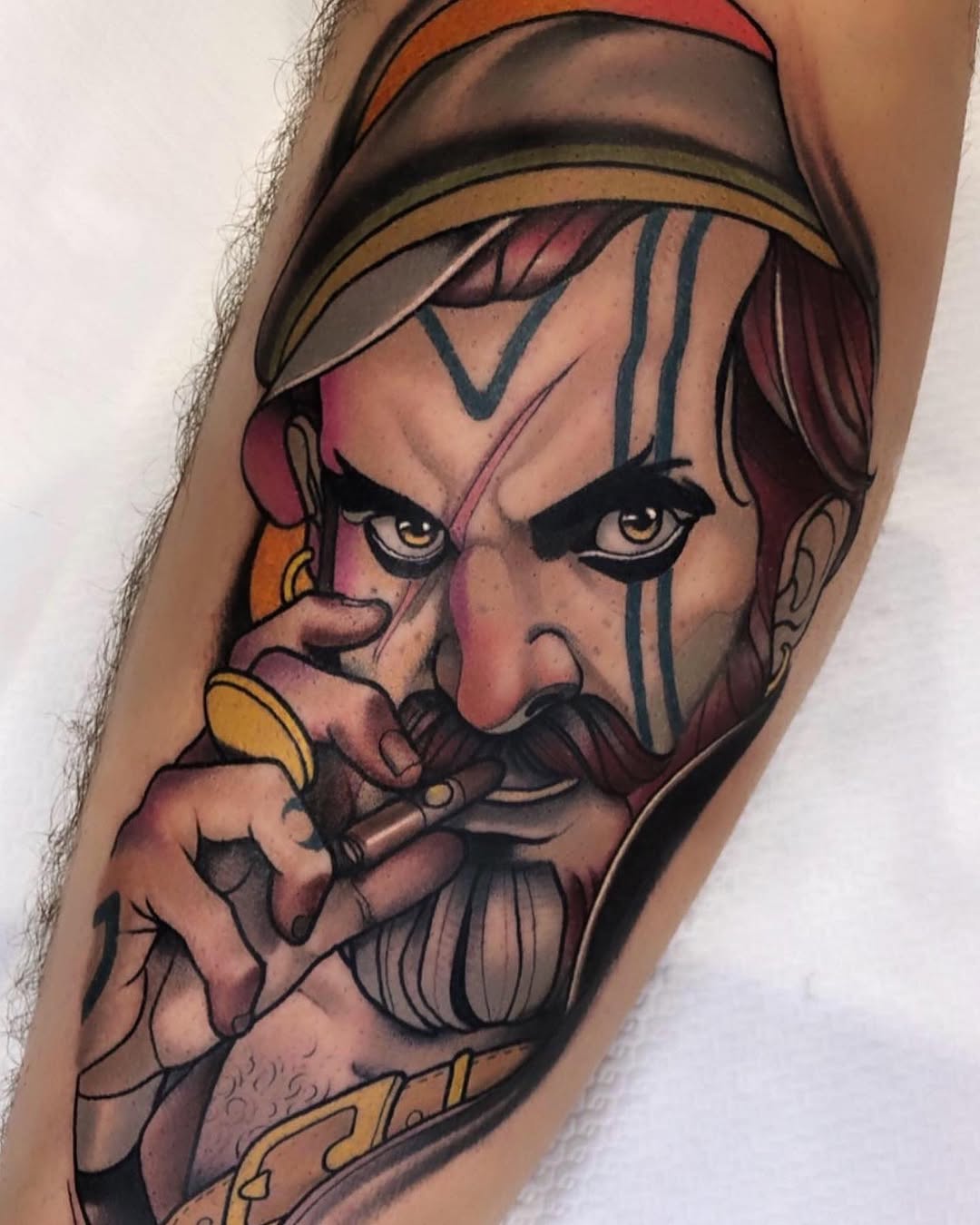 Colorful portrait tattoo of a bearded man with a headwrap, facial markings, and gold jewelry on the inner arm, featuring warm tones and detailed shading.