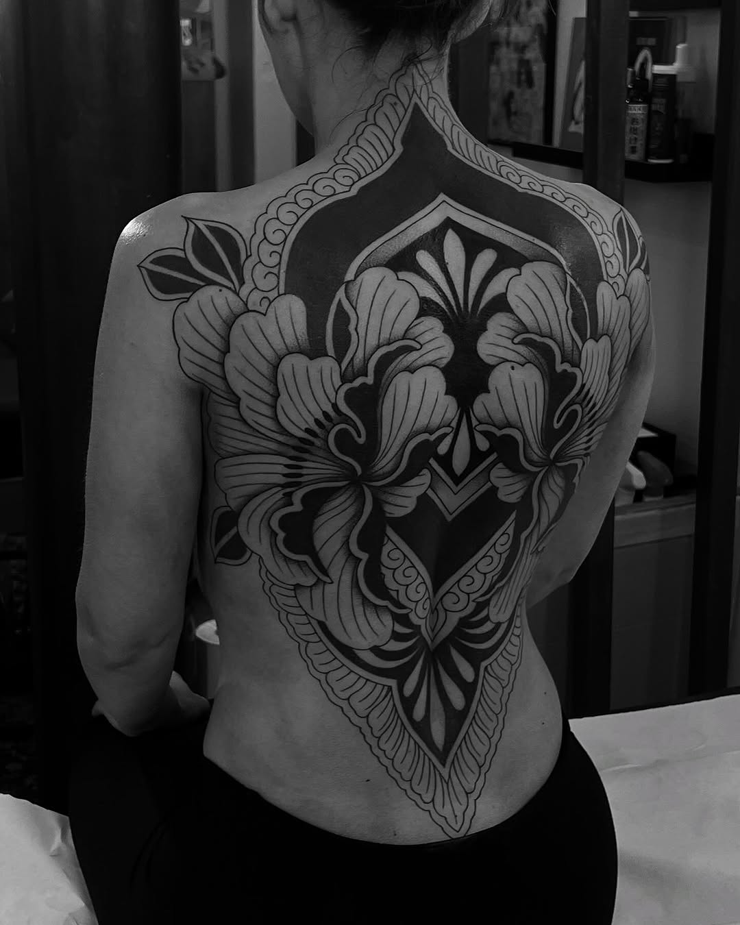 Back tattoo featuring a large symmetrical floral design with ornate geometric framing and decorative borders in black ink.
