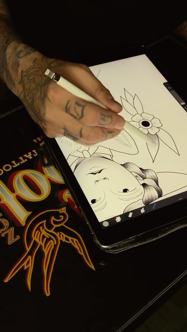 Tattooed arm holding tablet displaying line drawings of a flower and two female faces with closed eyes.
