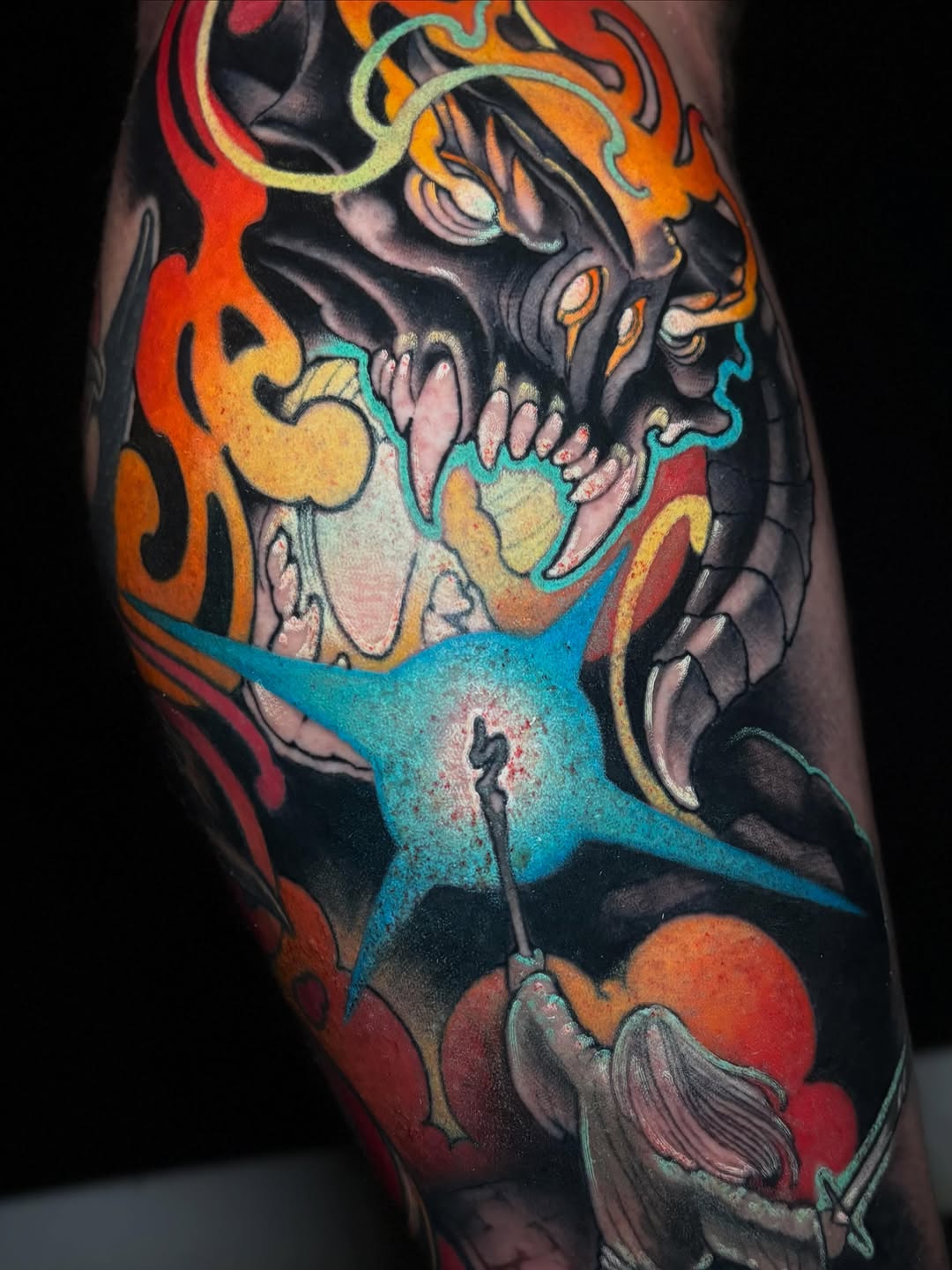Colorful demon skull tattoo on leg featuring orange flames, turquoise accents, and detailed facial features with red and yellow highlights.