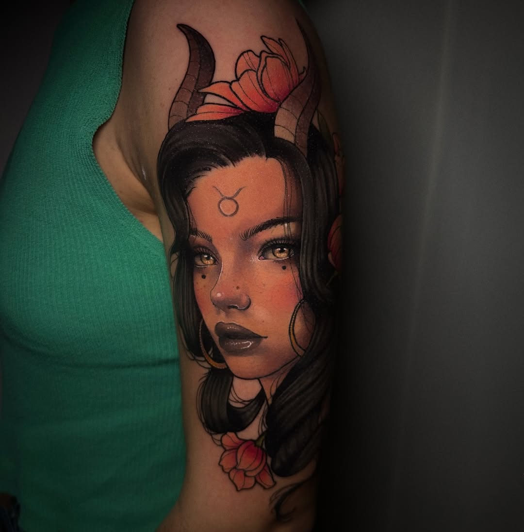 Colorful shoulder tattoo featuring a woman with horns, gold eyes, and facial markings, surrounded by red flowers and decorative elements.