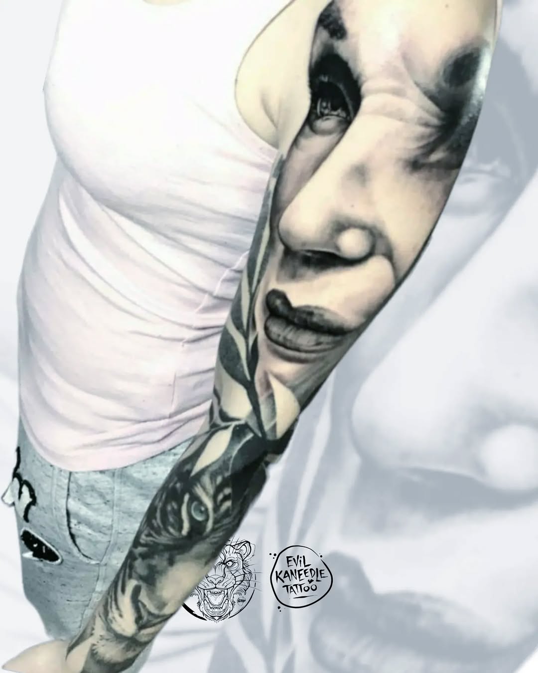 Detailed portrait tattoo on the inner arm featuring a face with expressive features rendered in black ink on pale skin.