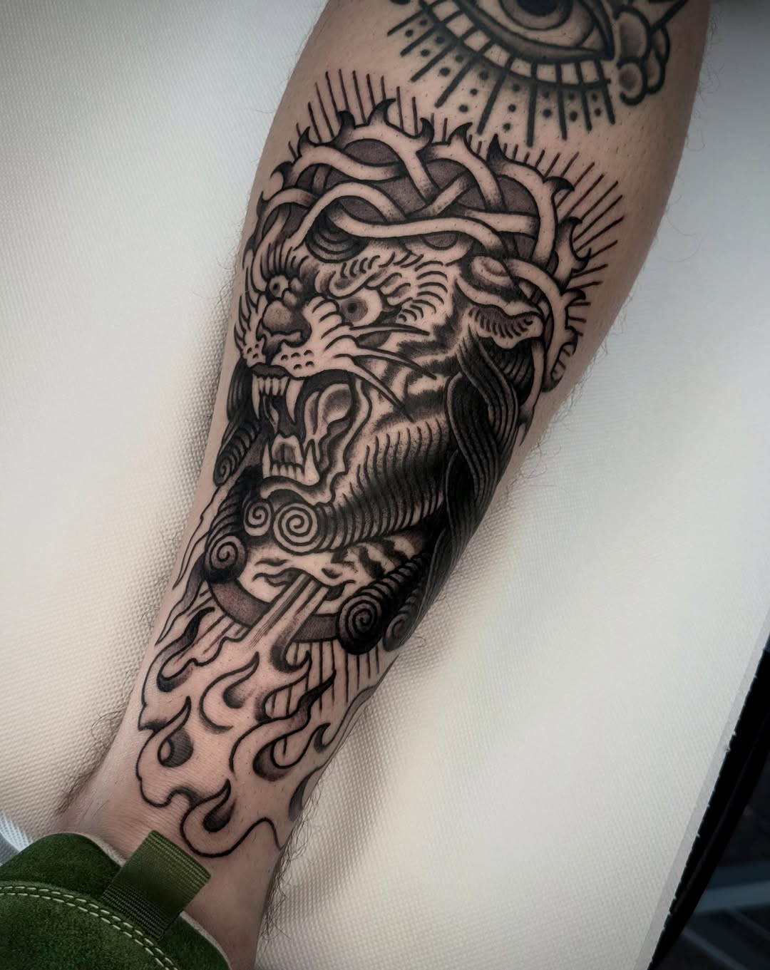 Bearded male head with serpents and ornamental details tattooed on a forearm in black ink with shading.