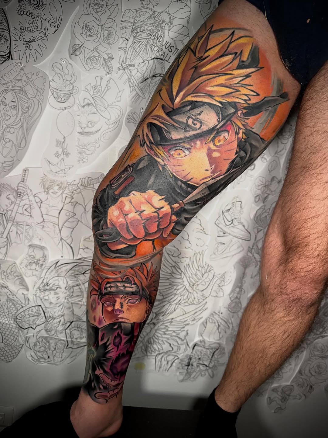 Colorful full-leg sleeve tattoo featuring an anime character with spiky hair and mask on the upper thigh, with additional character portraits below in orange, red, and purple tones.