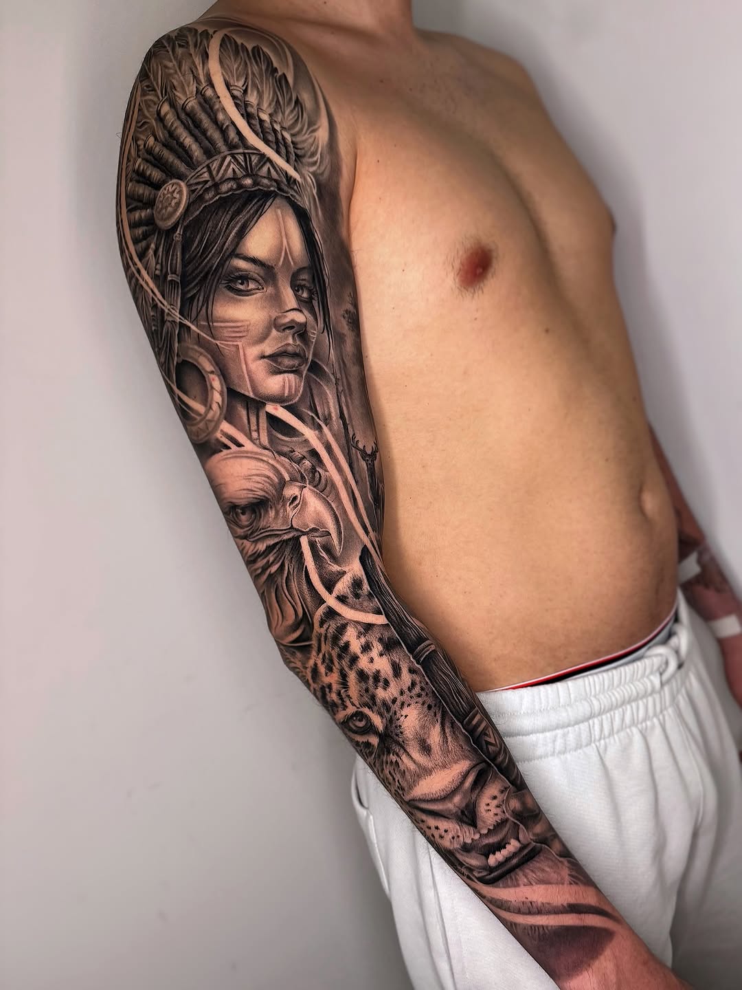 Full sleeve tattoo on male arm featuring a woman's portrait with elaborate headdress, leopard, and ornamental details in black and grey ink.