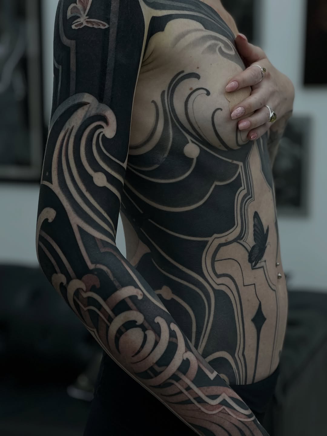 Full-sleeve tattoo featuring ornate scrollwork and curved flourishes in black and tan on a person's arm and torso.