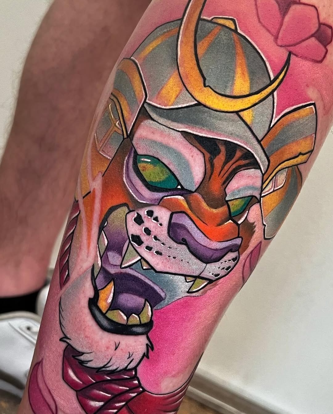 Colorful lion head tattoo on arm featuring orange, purple, pink, and teal tones with gold accents and black outlines.